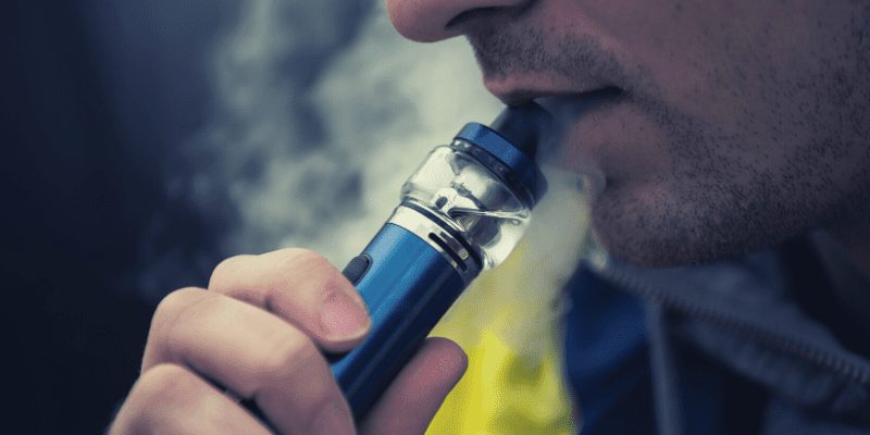 A person vaping a blue device, partially visible, smoke surrounding. Is it OK to inhale CBD?